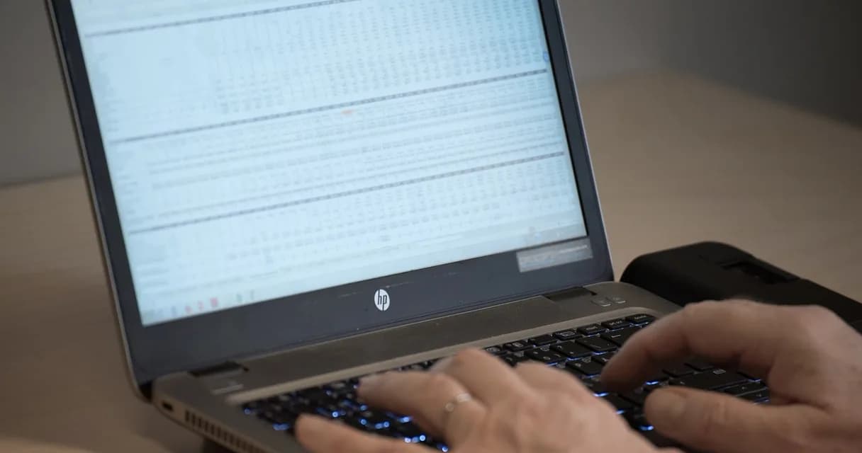 Mãos digitando em um notebook com uma planilha de dados na tela